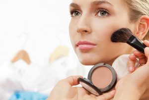 Using blush brush to apply blush on cheeks - professional makeup artist working